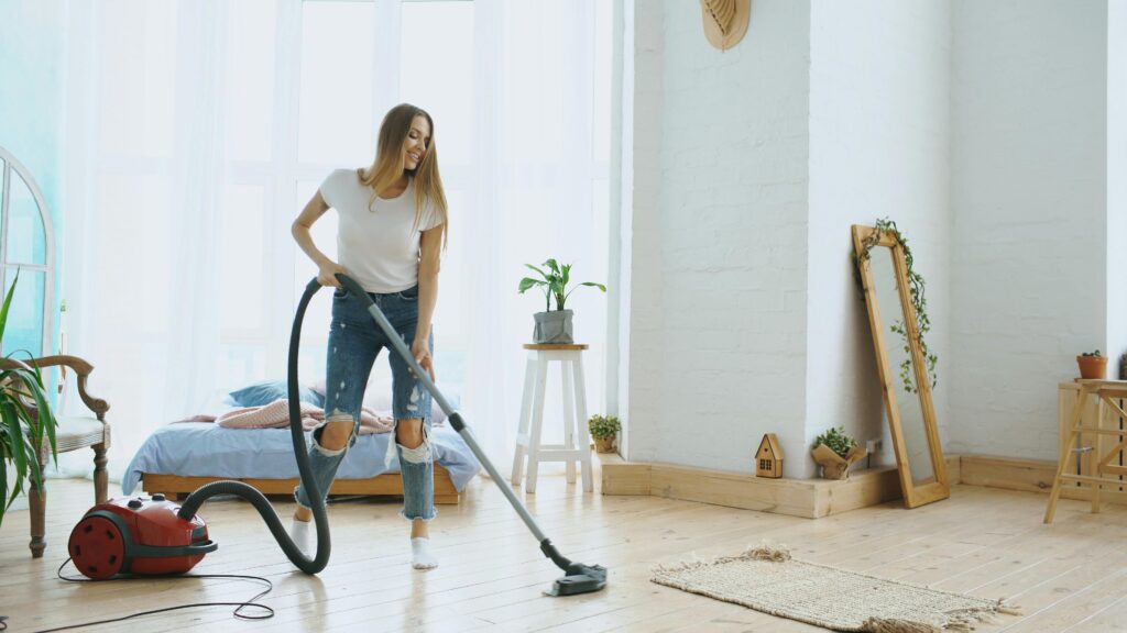 Young woman cleaning her bedroom with a vacuum cleaner, enjoying the tidy space.