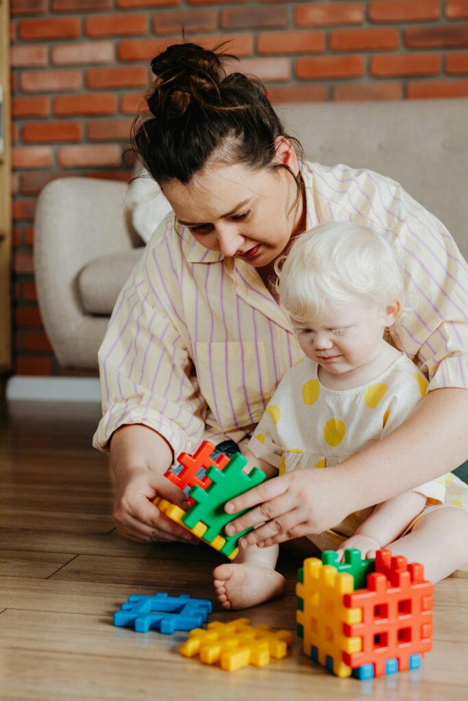 A mother and child enjoying playtime indoors with colorful building blocks on a wooden floor.